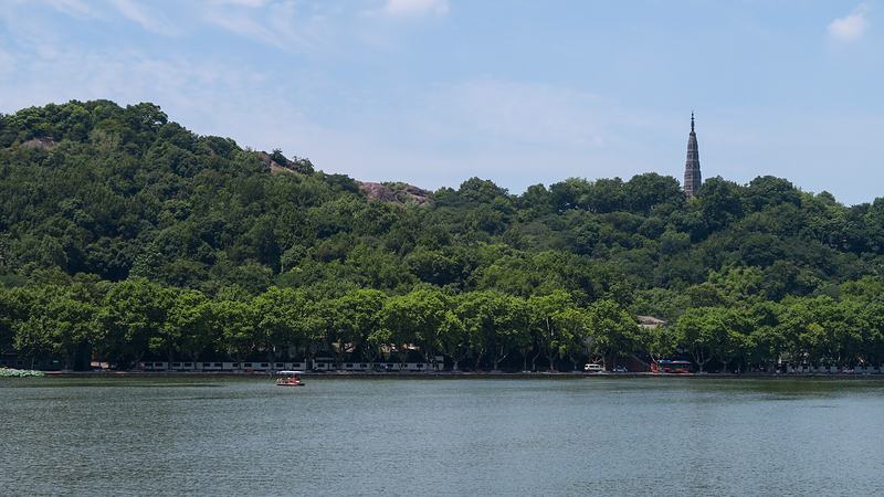Baochu Pagoda on a densely wooded hill above the lake, under a blue sky.