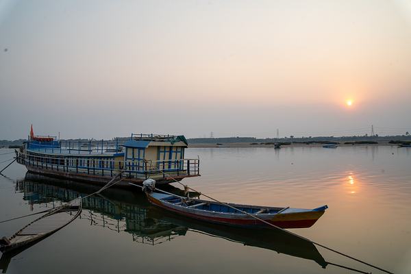 A two-decked ferry and a small wooden boat moored on the river at sunset.