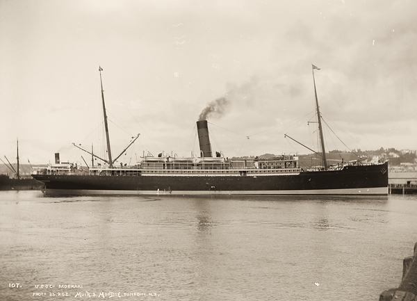 A two-masted steamship with a single funnel, lying in a harbour.