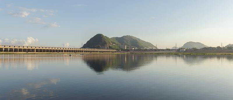 A long low barrage across a still river at dawn, with a rocky hill behind, all reflected in the water.