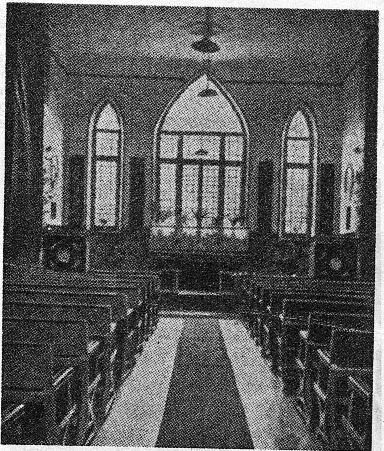 The inside of a plain chapel with rows of pews and tall pointed windows.