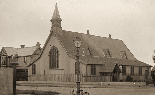 A large wooden church with a small bell turret, behind a street lamp.