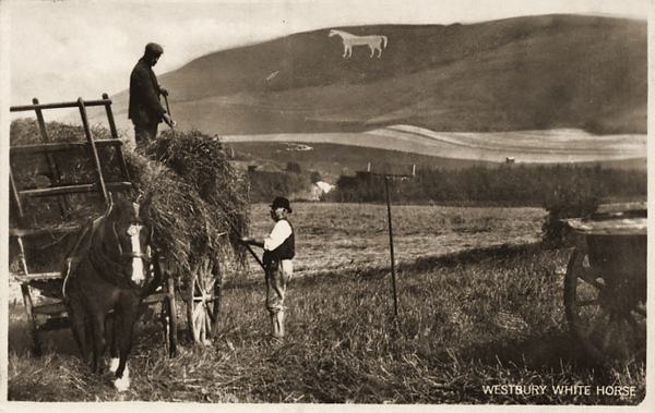 Two men loading hay onto a horse-drawn cart in a field, with the White Horse on the hill behind.